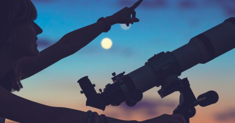 Silhouette of a female student who pointing something towards the black starry sky with a telescope.